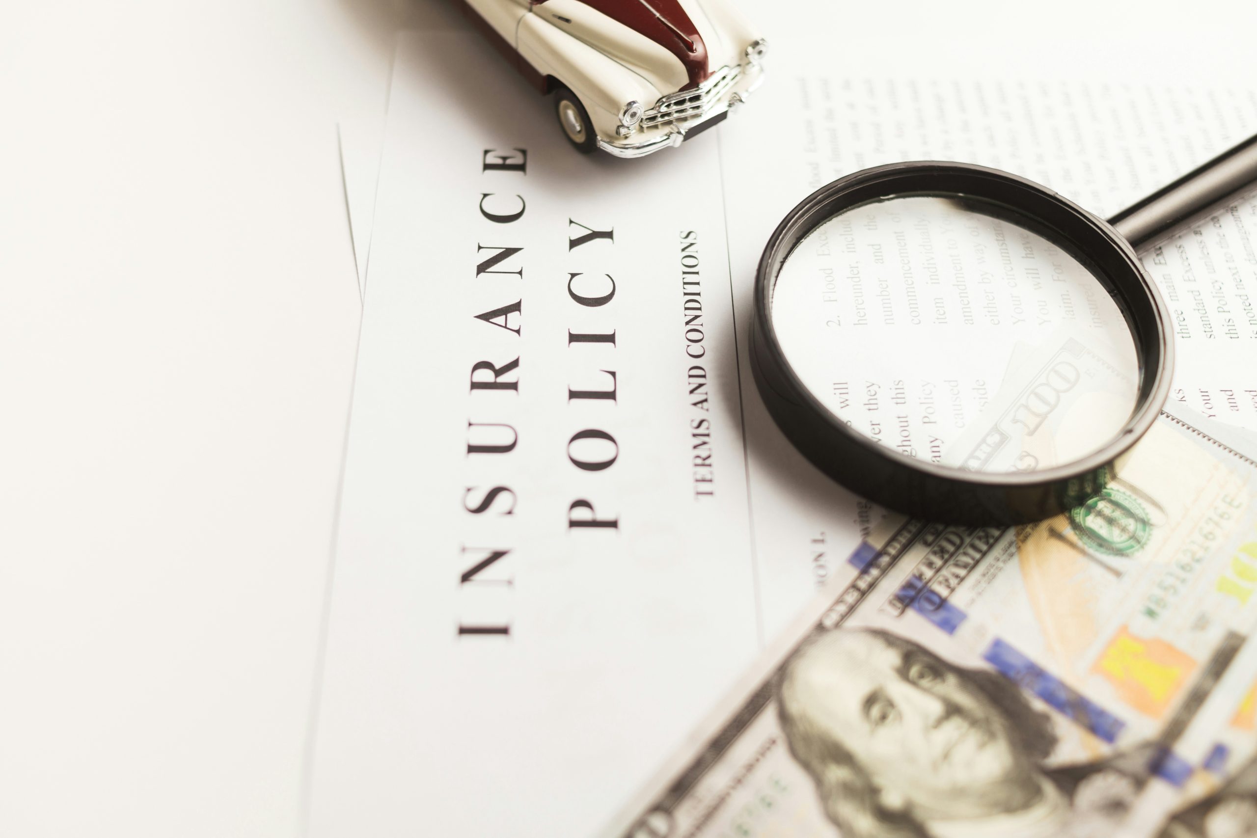 car insurance policy, toy car, magnifying glass, and dollar bills